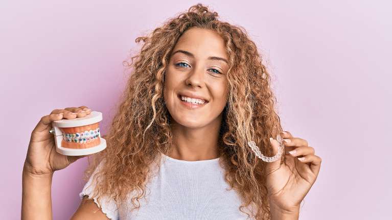 Smiling young woman holding braces model and clear aligner at Brentwood TN dental clinic